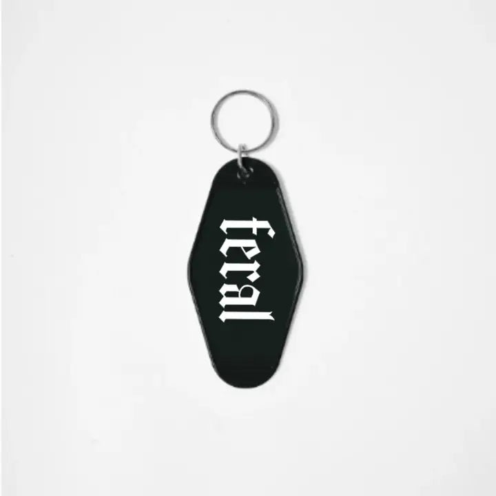 A black keychain shaped like a motel tag with the word "Feral" written in a white gothic font