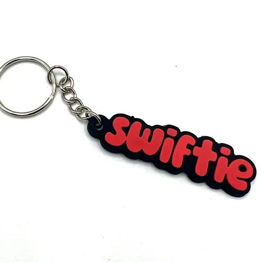 A rubber keychain of the word "Swiftie" written in a red font with a black outline
