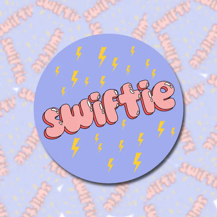 A circular light purple sticker with the word "Swiftie" in a pink font surrounded by designs of yellow lightning bolts