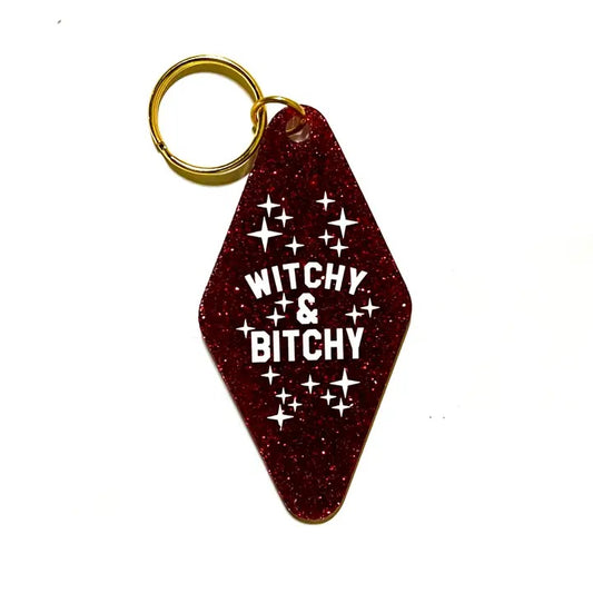 A red glitter keychain shaped like a motel tag with the words "Witchy & Bitchy" in a white font and white star decals around the words